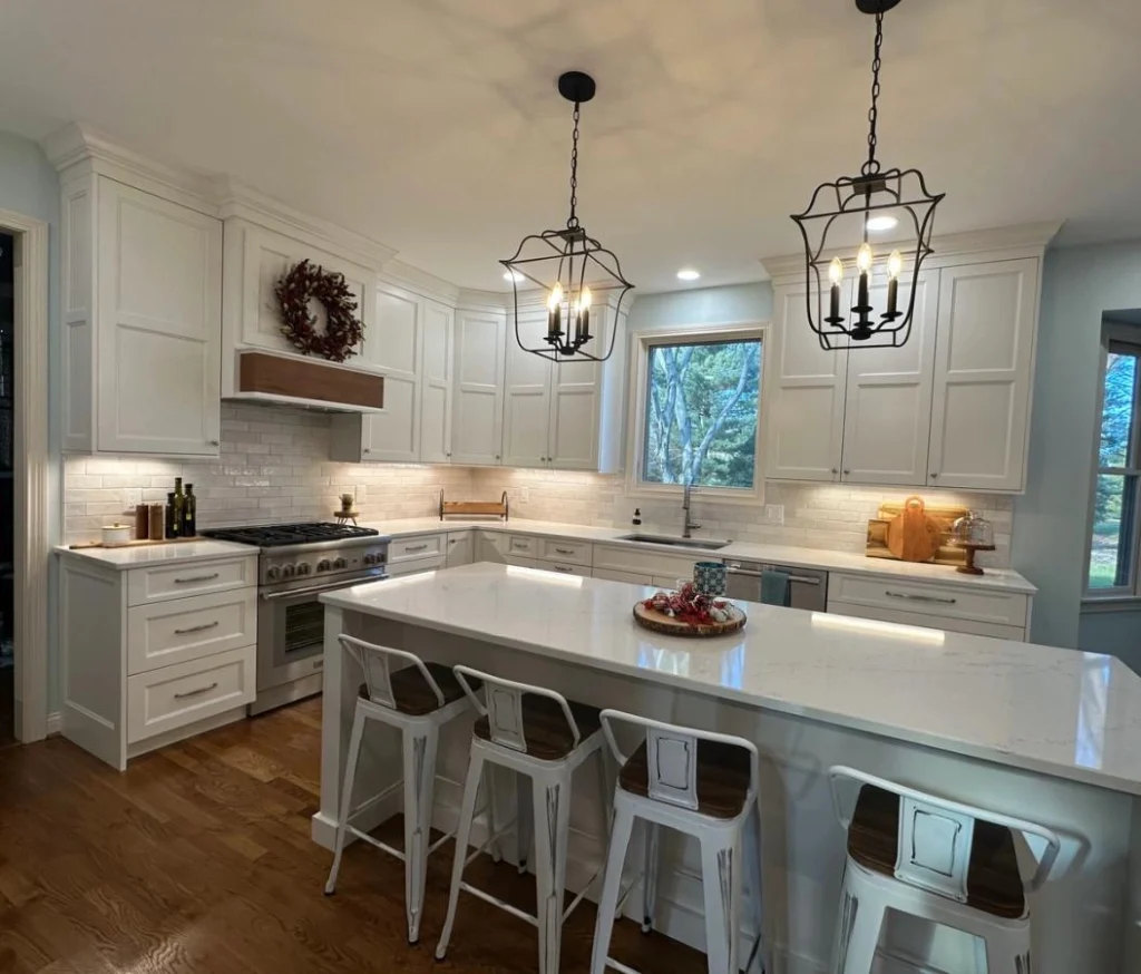 Bright kitchen with white shaker cabinets, stainless steel gas stove, marble-look countertops, subway tile backsplash, and medium-toned hardwood flooring.